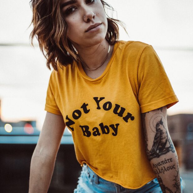 Mulher tatuada com os cabelos loiros com camiseta escrita not your baby