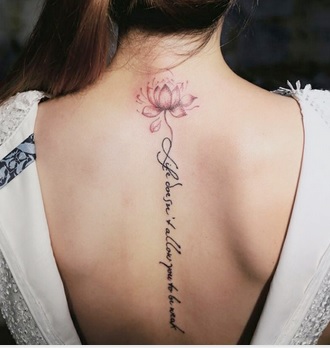 mulher com uma tatuagem de um escrito e uma flor de lótus nas costas.