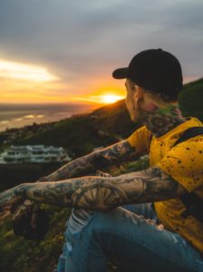 Homem-tatuado-olhando-a-paisagem-boné-preto-camisa-amarela-e- jeans-rasgado